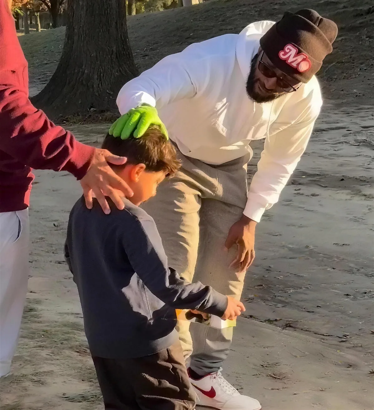 A coach in a Mo beanie helping a young golfer